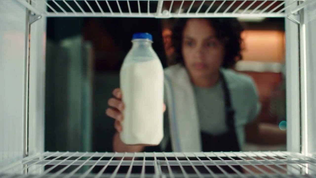 Seen through the fridge shelves, a baker holds up the last bottle of milk